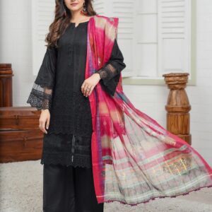 A woman in a black suit in a multi-color dupatta stands in a room in front of a window, posing for a photo shoot from the front of the black suit.